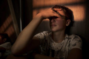 portrait of a teenager boy sitting in the dark room, with a beam of light over his eyes