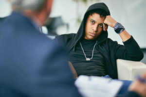 Black male adolescent listening to his counsellor during therapy session at psychotherapist's.